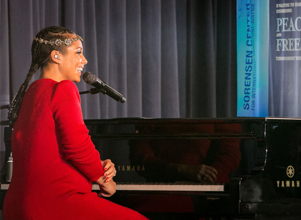 Alicia Keys smiling while sitting at a piano at the Sorensen Center opening